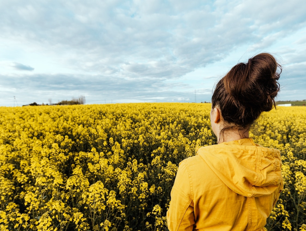 Femme en jaune au milieu d’un champ observant la nature lors d’une balade