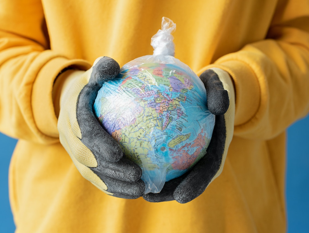 Mains avec des gants de ménage tenant une planète Terre emballée dans un sac en plastique pour illustrer la pollution