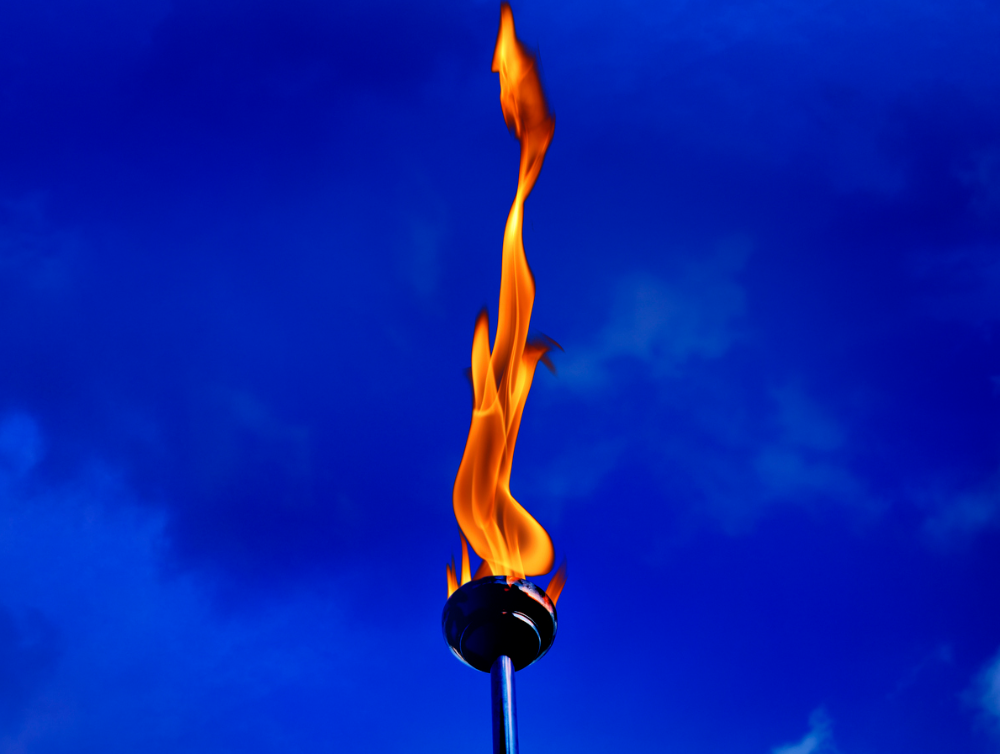 Bouchent main tenant une torche enflammée combustion avec flammes sur ciel bleu nuageux