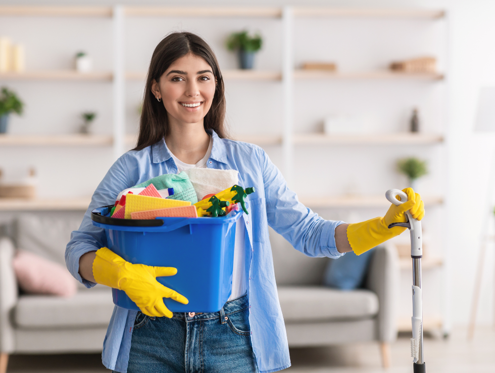 Joyeuse jeune femme au foyer tenant un seau avec des produits de nettoyage