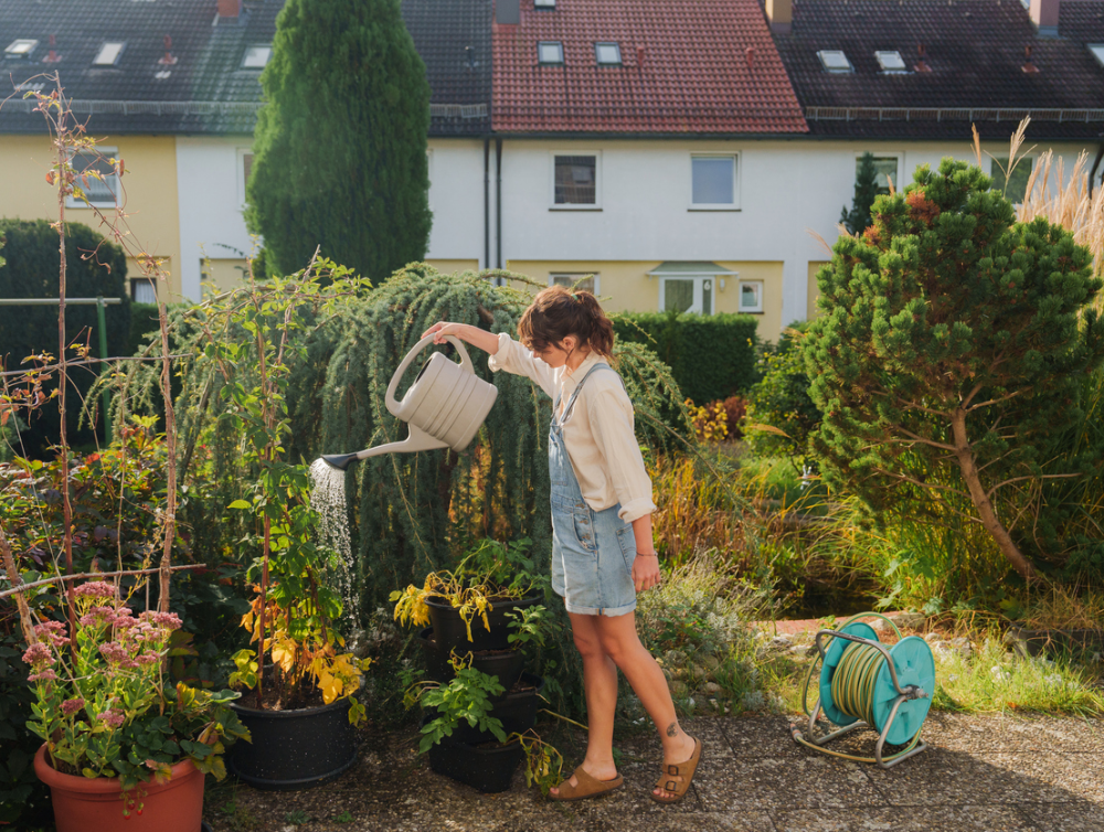 Woman in denim overalls watering plants on her backyard