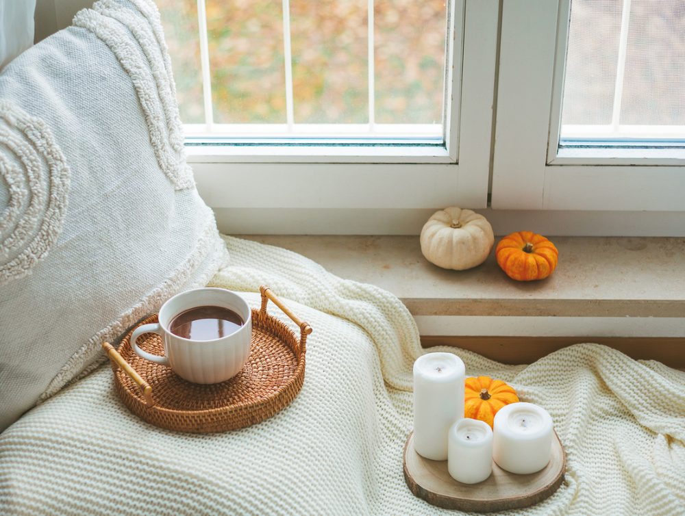 Cup of hot cocoa on a wicker rattan tray near the window, a plaid, a pillow, pumpkins. Eco home